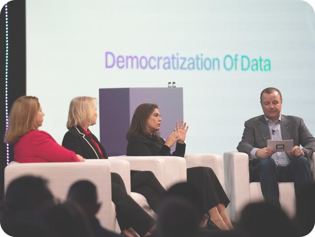Panel discussion on "Democratization of Data" with three women and one man seated on stage, engaged in conversation.